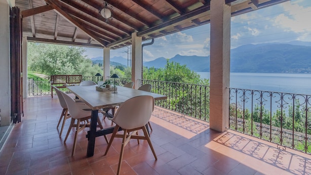 A covered outdoor dining area with a table and chairs, overlooking a body of water and mountains. - Villa Bianca Lierna by Varenna Holidays (Varenna)