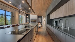 A modern kitchen with a long island, stainless steel appliances, and a view of the outdoors. - Modern Marvel - Incline Village - TLUXP (Incline Village)