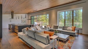 A modern living room with a large sectional sofa, a coffee table, and a dining area with a kitchen in the background. - Modern Marvel - Incline Village - TLUXP (Incline Village)