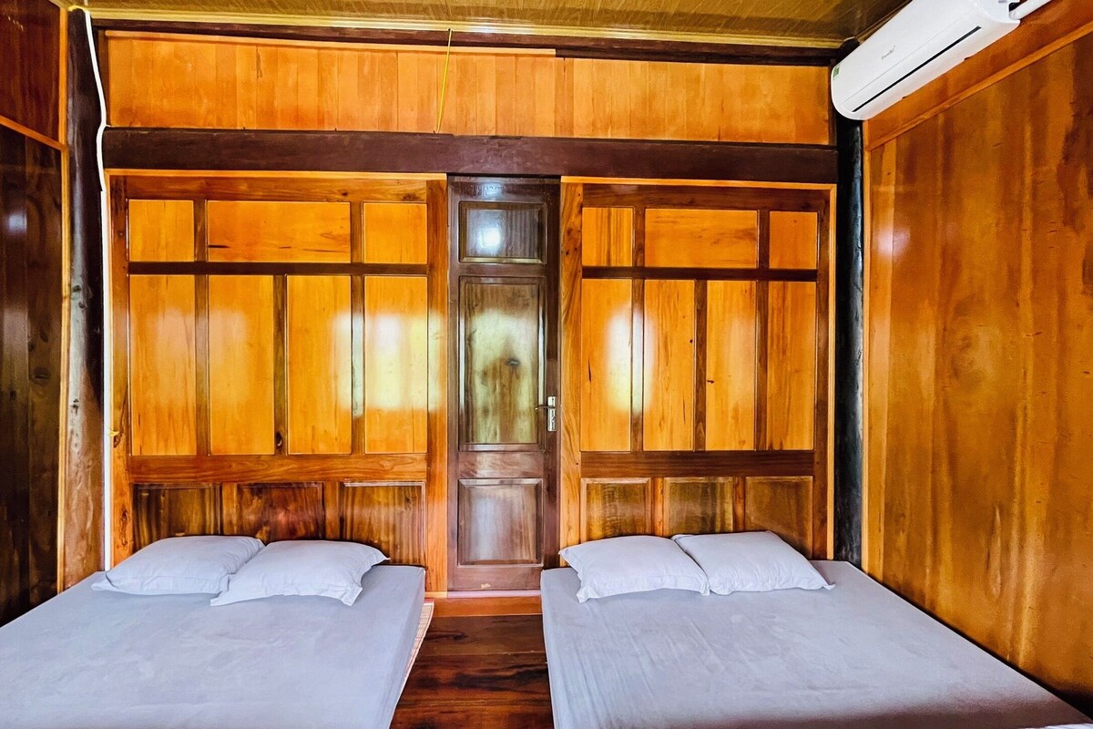 A room with two beds, wooden paneling, and an air conditioning unit.