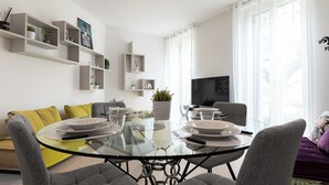 Una sala de estar moderna con una mesa de comedor de vidrio, sofás grises y un televisor en la pared.