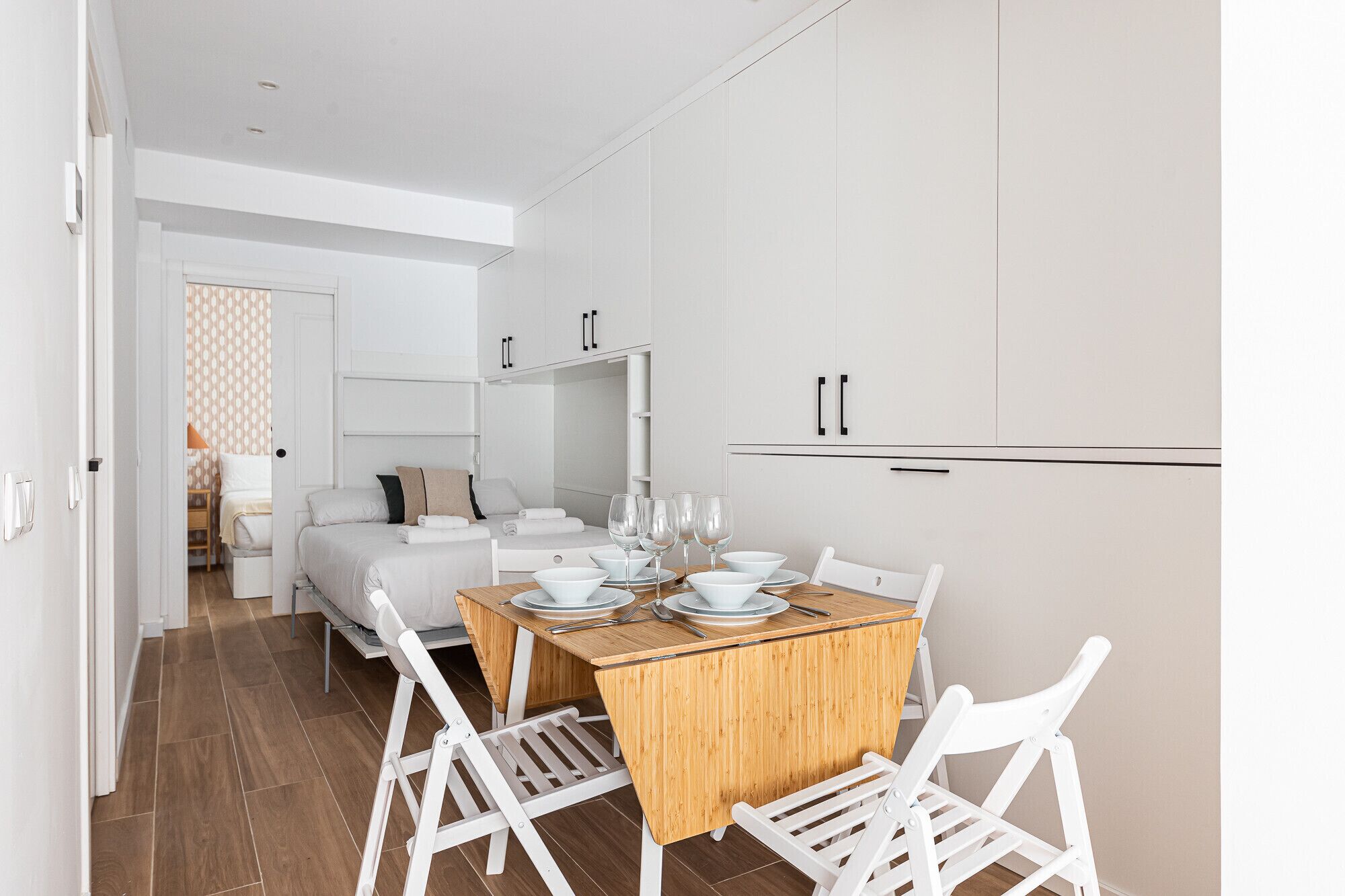 Een moderne, minimalistisch ingerichte kamer met een eethoek, bestaande uit een houten tafel en witte stoelen.