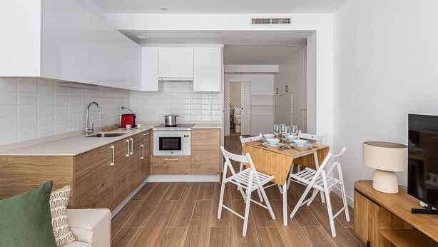 Une cuisine moderne avec des meubles blancs, un plan de travail en bois et un coin repas comprenant une table et des chaises.