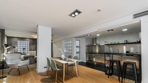 Una cocina moderna con electrodomésticos de acero inoxidable, una zona de comedor con una mesa y sillas de madera, y una barra con taburetes.