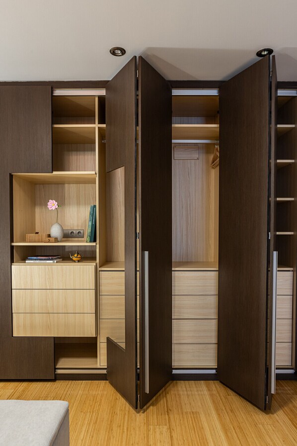 A room with a built-in wardrobe, a small desk with a vase and books, and a wooden floor.