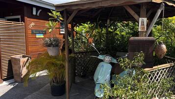 Un espace extérieur abrité, avec des sièges, où est garé un scooter, le tout entouré de plantes en pot et d’une clôture en bois.