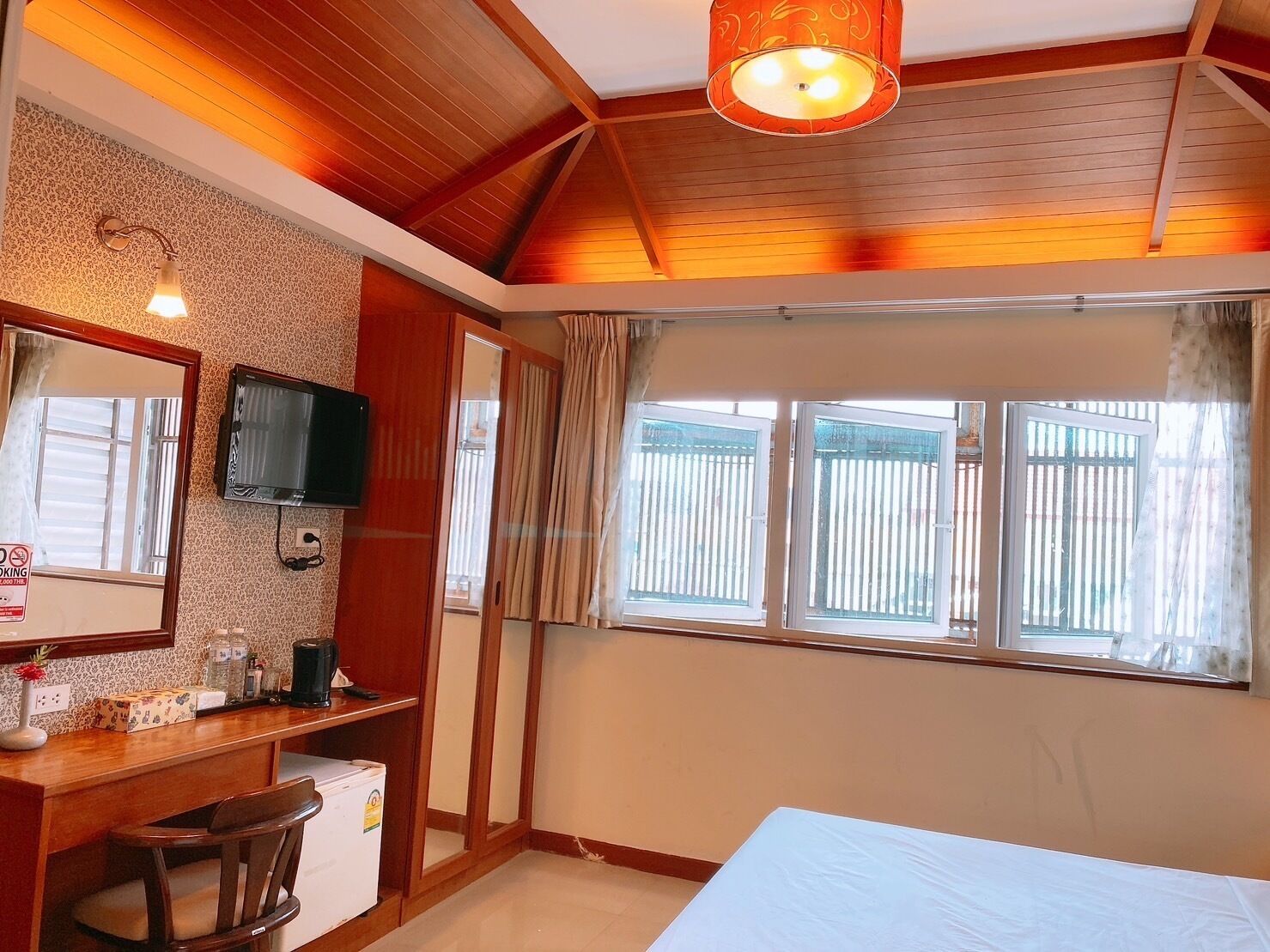 A bedroom with a bed, a desk, a chair, a TV, and a window with curtains.