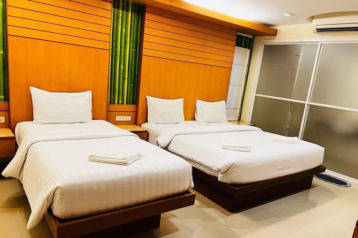 Une chambre d’hôtel avec deux lits, des têtes de lit en bois, une grande fenêtre avec des rideaux verts et une armoire.