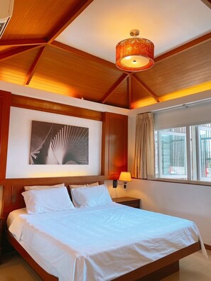 Une chambre d’hôtel avec un plafond en bois, un lit avec du linge de maison blanc, une œuvre d’art accrochée au mur, une lampe de chevet et une fenêtre avec des rideaux.