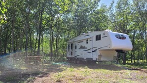 A white RV with a camper shell parked in a forested area. - The Riverside Windchaser!  (Petit Étang)