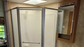 A compact RV bathroom with a shower enclosure, a sink, and a mirror. - The Riverside Windchaser!  (Petit Étang)