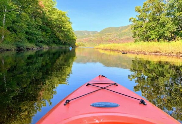 A red kayak on calm water with a clear view of a river surrounded by greenery.