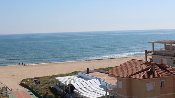 A coastal view with a beach, a building with a tiled roof, and a clear sky. - Jardín II, 5º Solo Familias (Xeraco Playa)