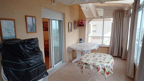 A balcony with a covered grill, a table with a fruit pattern tablecloth, and a view of the outside.