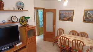 A dining area with a table set for four, a television on a wooden stand, and a door leading to another room.