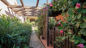 A stone pathway leading to a wooden pergola with a view of a building in the background.