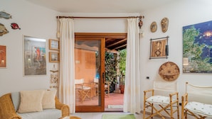 A cozy living room with a wicker sofa, a small table with a cup, and a sliding glass door leading to an outdoor patio with chairs and plants.