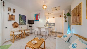 A modern living room with a sofa, dining table, and chairs, a kitchen area, and a TV.