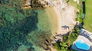 An aerial view of a coastal property with a swimming pool, a beach, and a wooden deck.