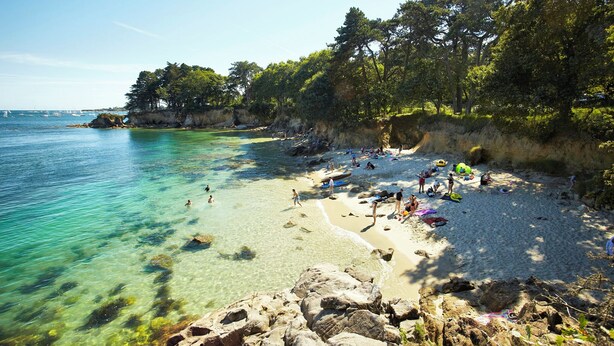 A beach with clear turquoise water, rocky shoreline, and people sunbathing. - Maison Bretonne Typique Plage des Oiseaux à Fouesnant Beg Meil (Fouesnant)