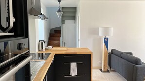 A modern kitchen with a wooden countertop, black cabinetry, and a stainless steel range hood. A staircase leads to a living area with a grey sofa and a lamp. - Maison Bretonne Typique Plage des Oiseaux à Fouesnant Beg Meil (Fouesnant)
