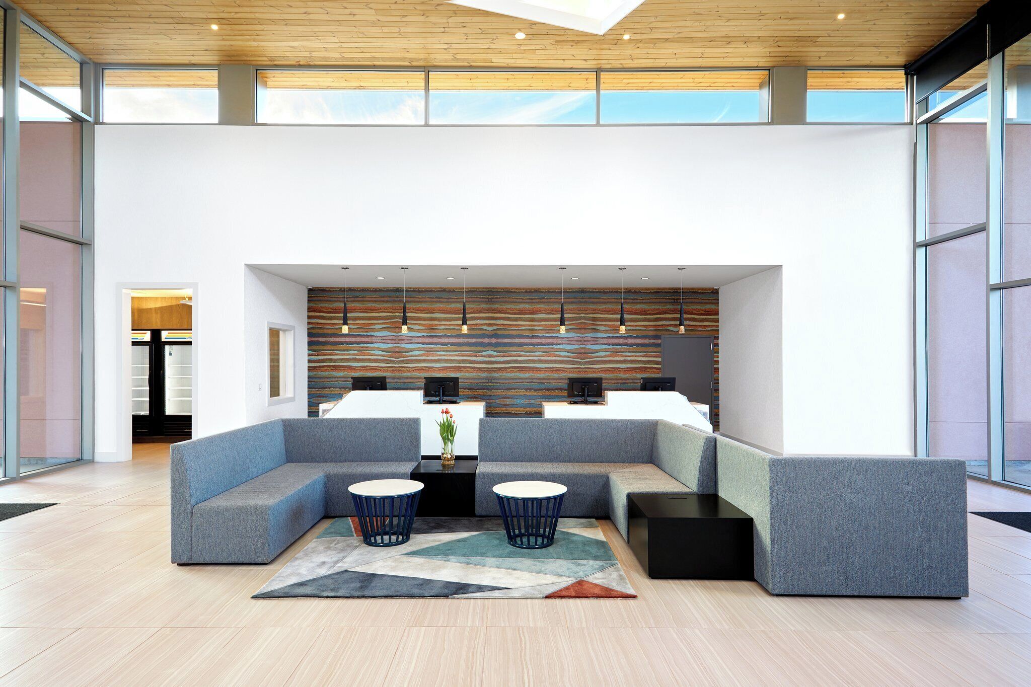 A modern lobby with a sectional sofa, two round tables, and a patterned wall.
