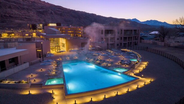 Un resort con una amplia piscina exterior, sillones de descanso y montañas al fondo.