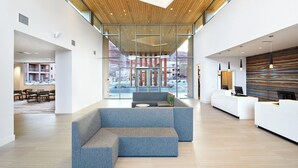Un hall amplio con diseño moderno, que incluye un sofá modular azul, un mostrador de recepción y un gran ventanal con vistas al exterior.