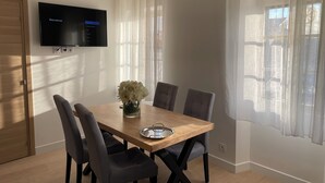 A dining area with a wooden table, grey chairs, a vase with flowers, and a TV mounted on the wall. - 2 Bedroom Apartment in Antibes (Antibes)