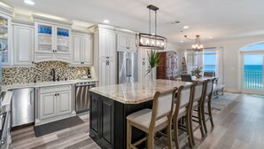 A modern kitchen with white cabinetry, a central island with bar stools, stainless steel appliances, and a view to the outside. - Incredible 4BD, 3BA, GULF-FRONT, LG. PATIO, POOL, GRILL, PRIVATE BEACH (Santa Rosa Beach)