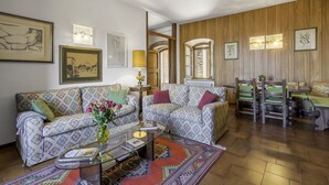A living room with patterned sofas, a coffee table with books, and a dining area with wooden chairs and a table. - Casa Martina, Piazza Delle Erbe, San Gimignano (San Gimignano)