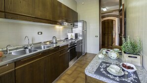 A kitchen with wooden cabinets, stainless steel appliances, a granite countertop, and a view of a wooden door. - Casa Martina, Piazza Delle Erbe, San Gimignano (San Gimignano)