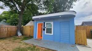 Un petit bâtiment d’un seul étage, à l’extérieur bleu et à la porte orange. On y voit un panneau avec un numéro au-dessus de la porte, une fenêtre avec des stores et un petit porche.