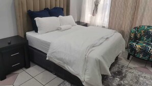 A bedroom with a bed, a nightstand, a chair, and a painting on the wall. - Saba Saba Guest House (Pretoria)