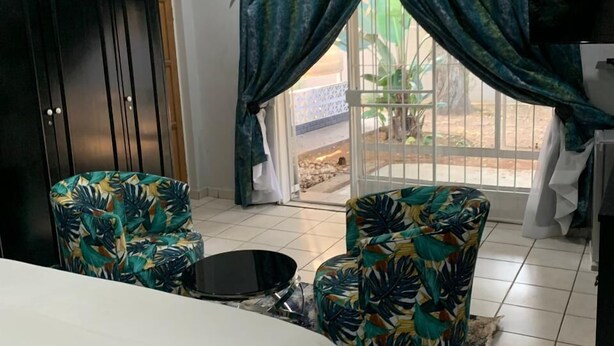 A bedroom with a bed, two chairs, a small table, a TV, and a window with curtains. - Saba Saba Guest House (Pretoria)