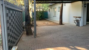 A covered outdoor area with a paved walkway, a metal fence, and a tree. - Saba Saba Guest House (Pretoria)