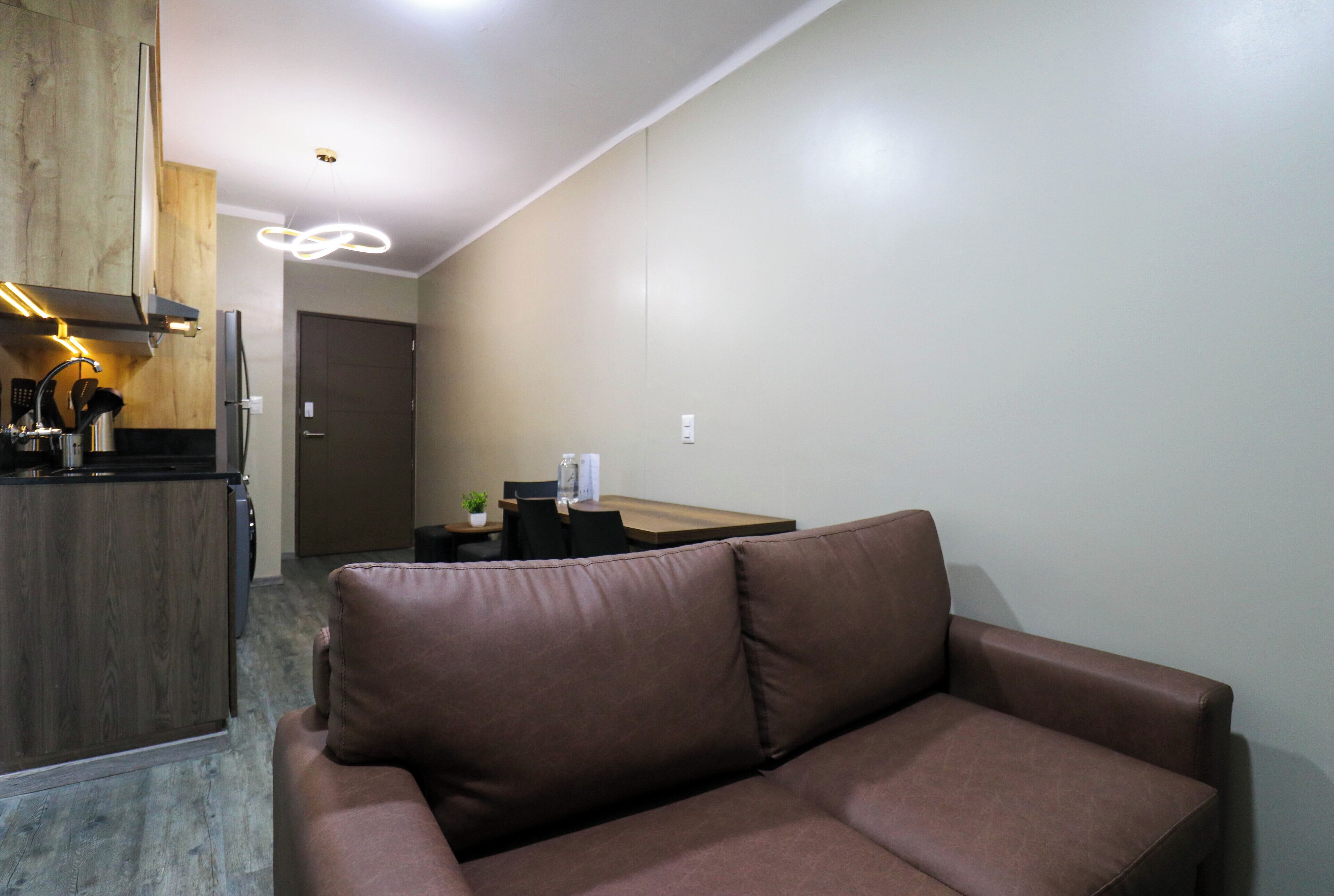 A modern living room with a brown leather sofa, a wooden cabinet, and a dining area with a table and chairs.