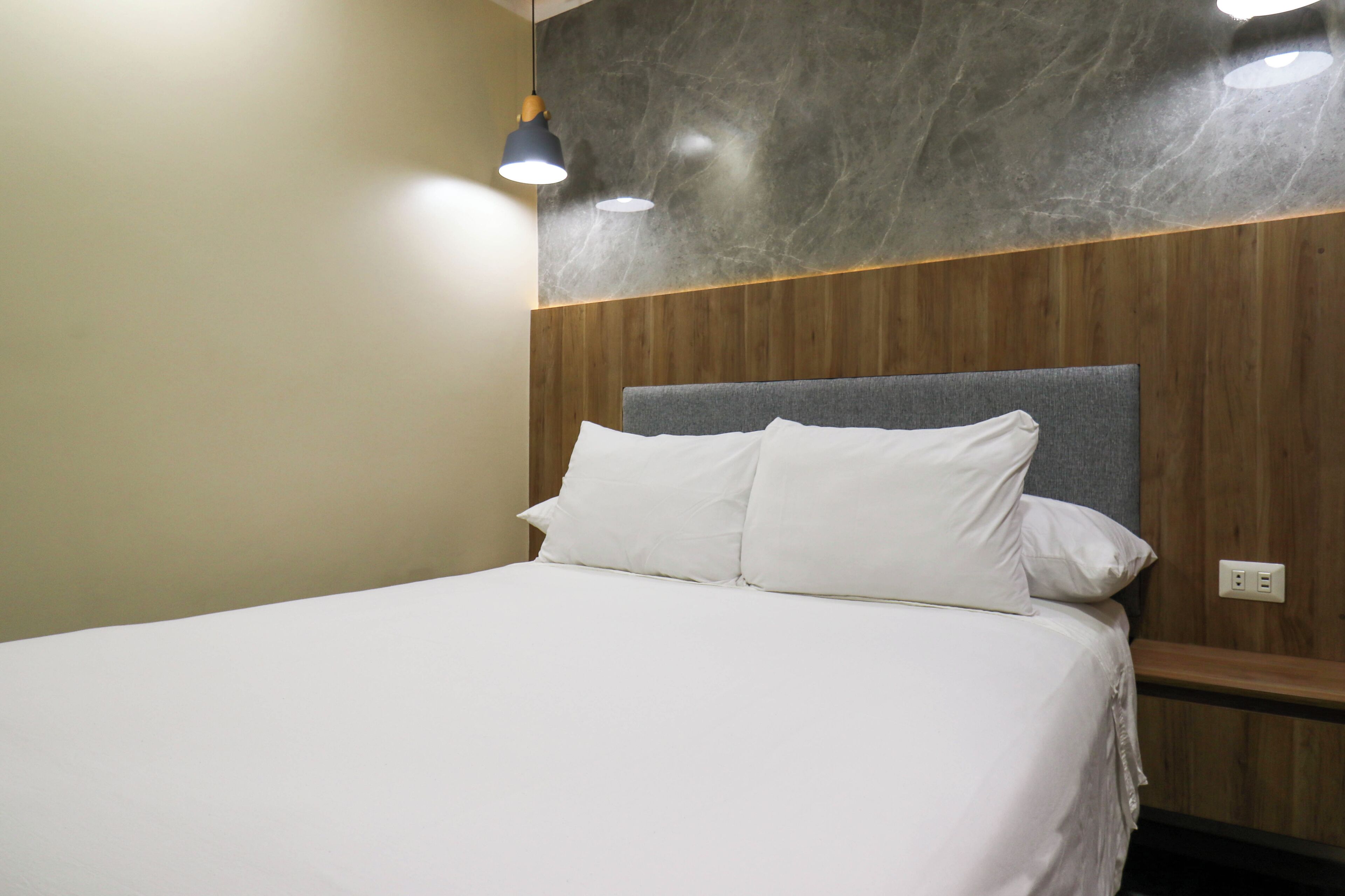 Una cama bien hecha con sábanas blancas en una habitación con paneles de madera y una pared de mármol.
