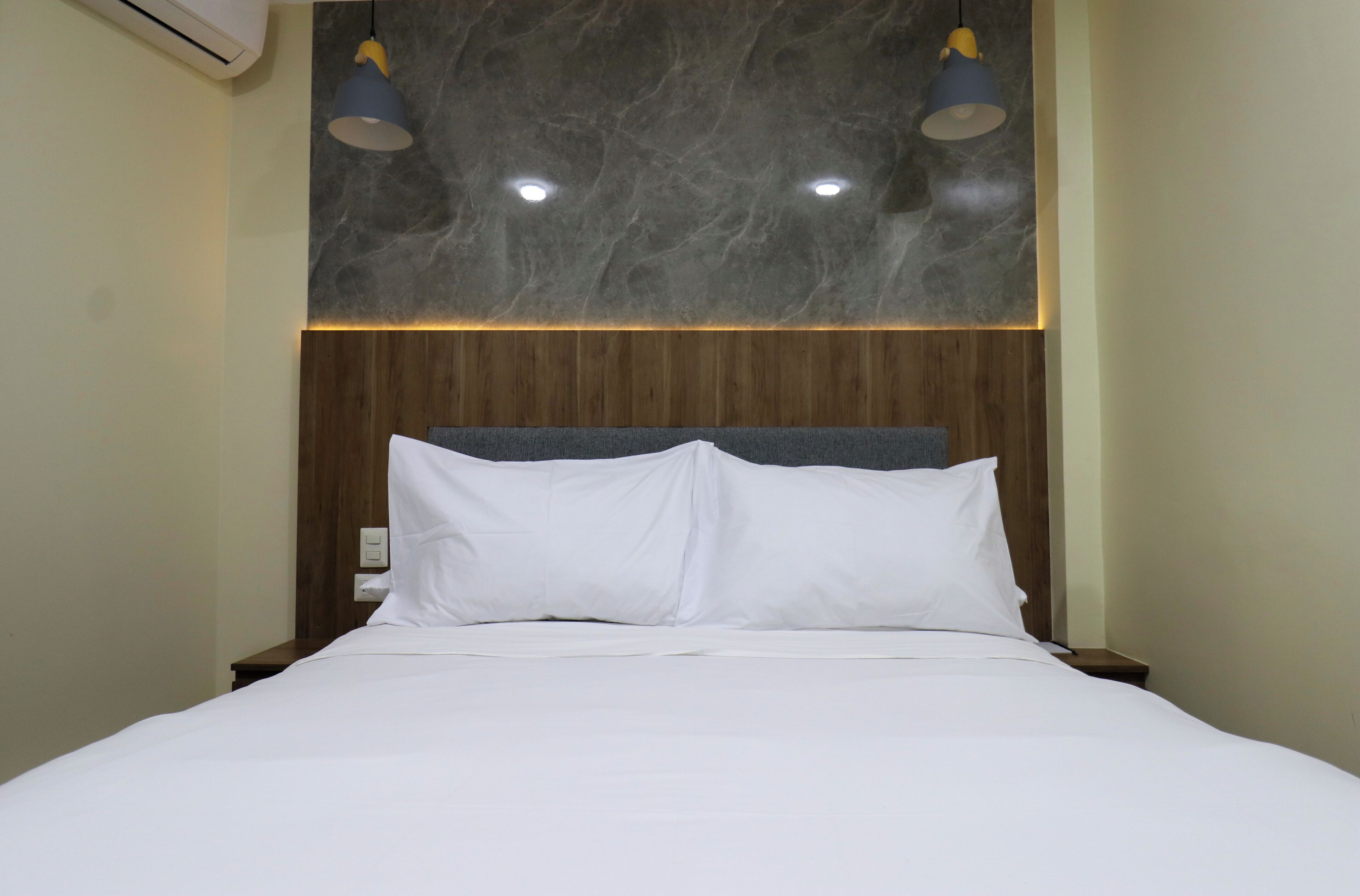 Une chambre d’hôtel avec un lit, une tête de lit en bois et deux lampes suspendues.