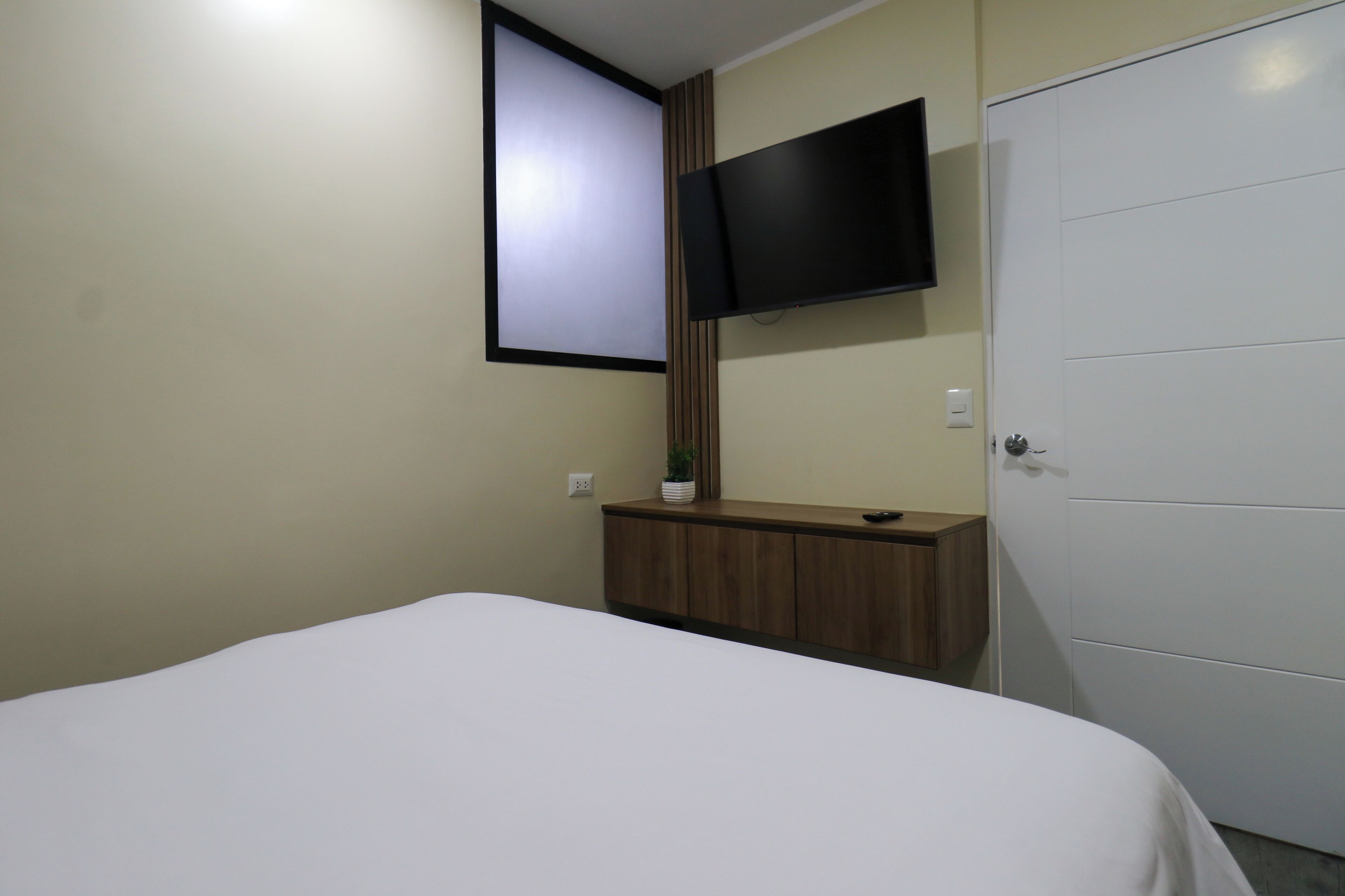 Une chambre à coucher avec un lit, un téléviseur fixé au mur, une armoire en bois et une garde-robe blanche.