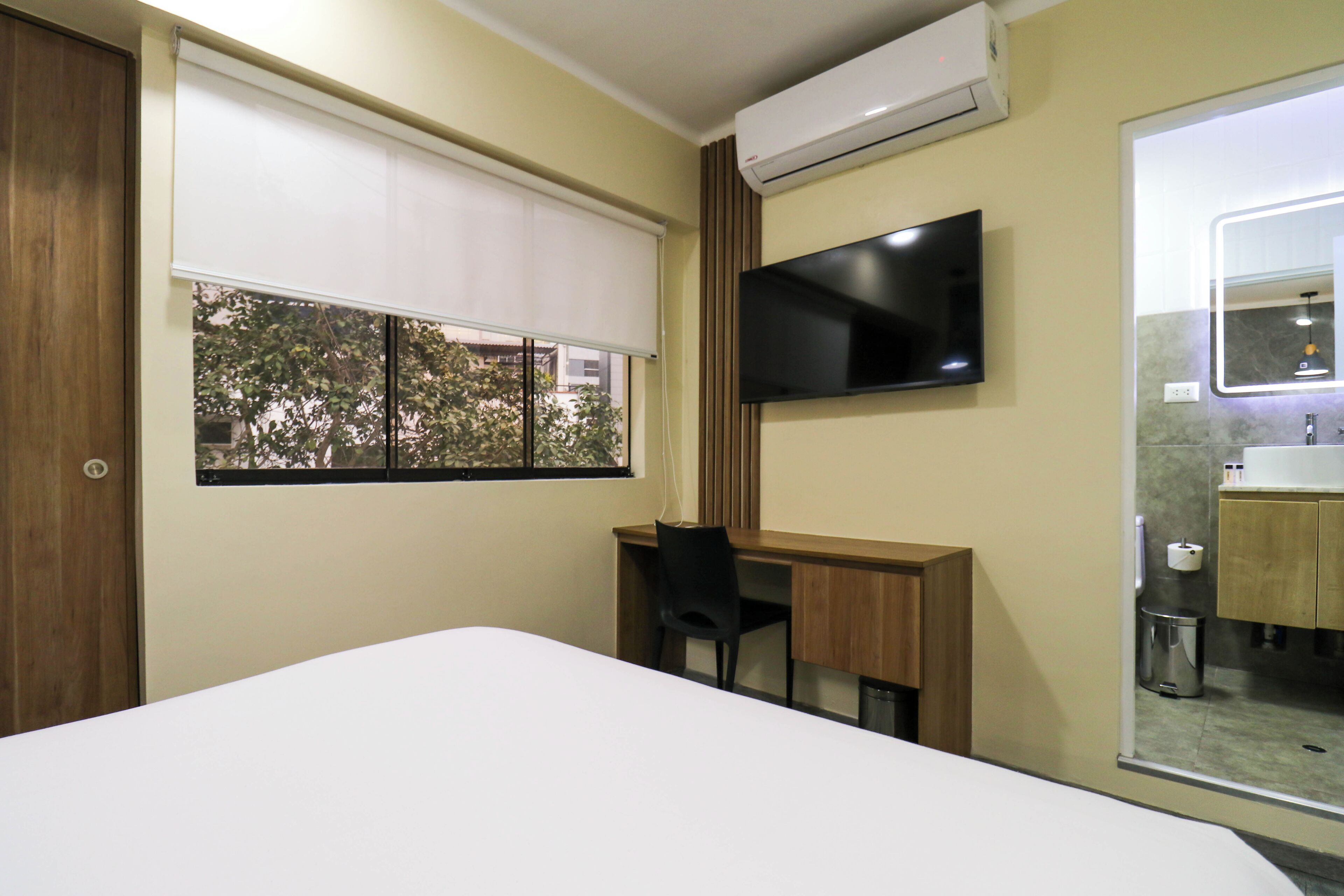 Une chambre d’hôtel comprenant un lit, un bureau, une chaise, une télévision et une salle de bain avec un miroir et un lavabo.
