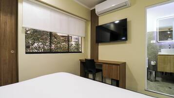 Une chambre d’hôtel comprenant un lit, un bureau, une chaise, une télévision et une salle de bain avec un miroir et un lavabo.