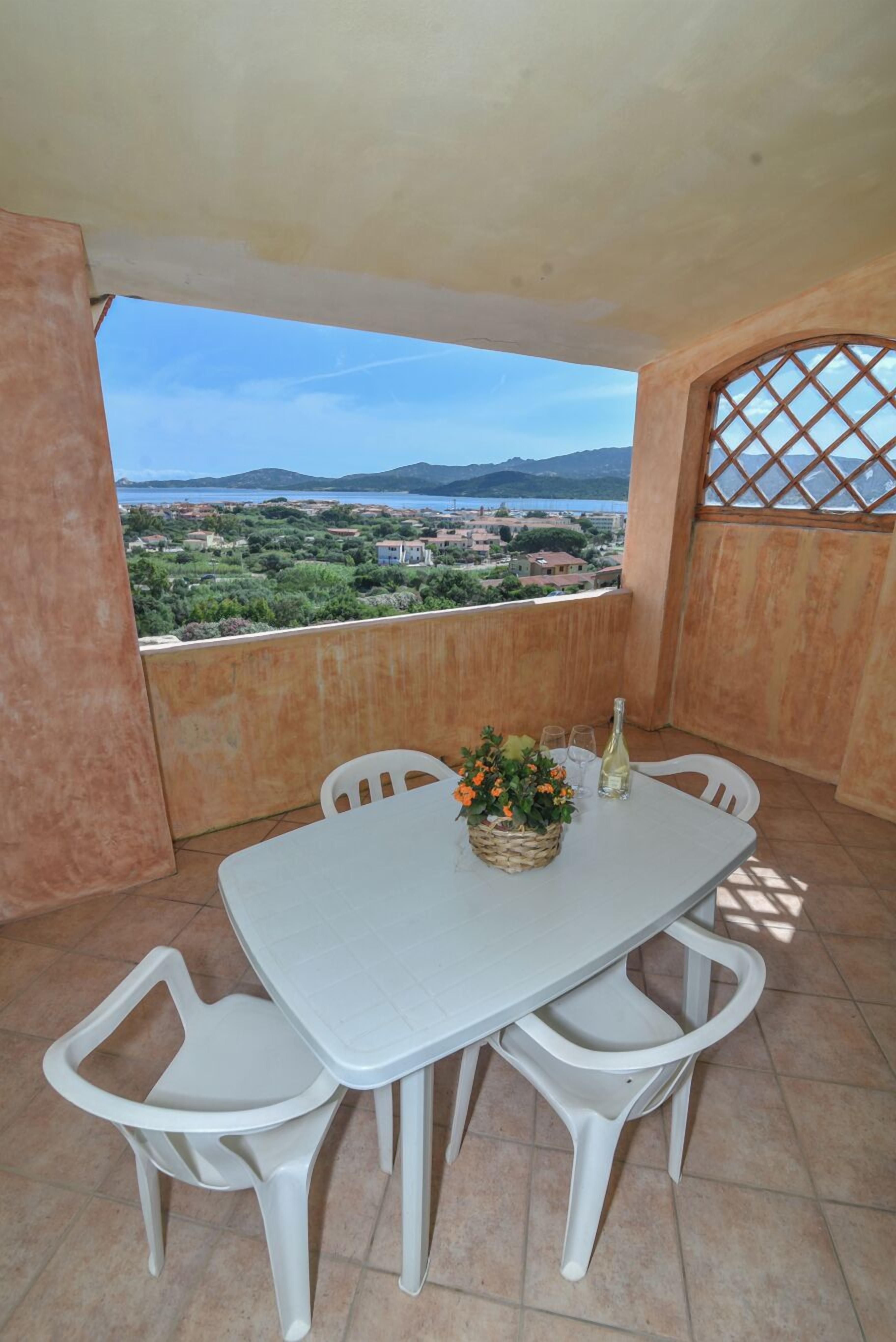 A balcony with a white table and chairs, a wicker basket with flowers, and a bottle of wine.