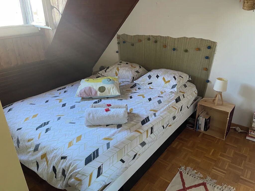 Ein Schlafzimmer mit einem Bett, Kissen, einem Nachttisch mit Lampe und Holzboden.