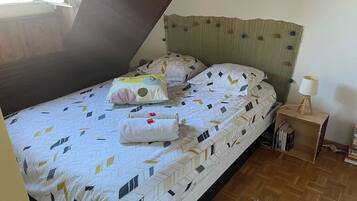 Ein Schlafzimmer mit einem Bett, Kissen, einem Nachttisch mit Lampe und Holzboden.