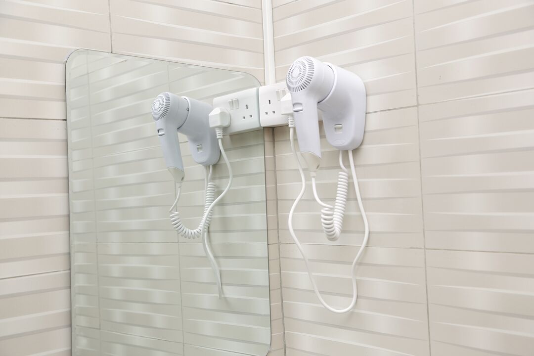 A bathroom with two hair dryers mounted on the wall, connected to a power outlet.
