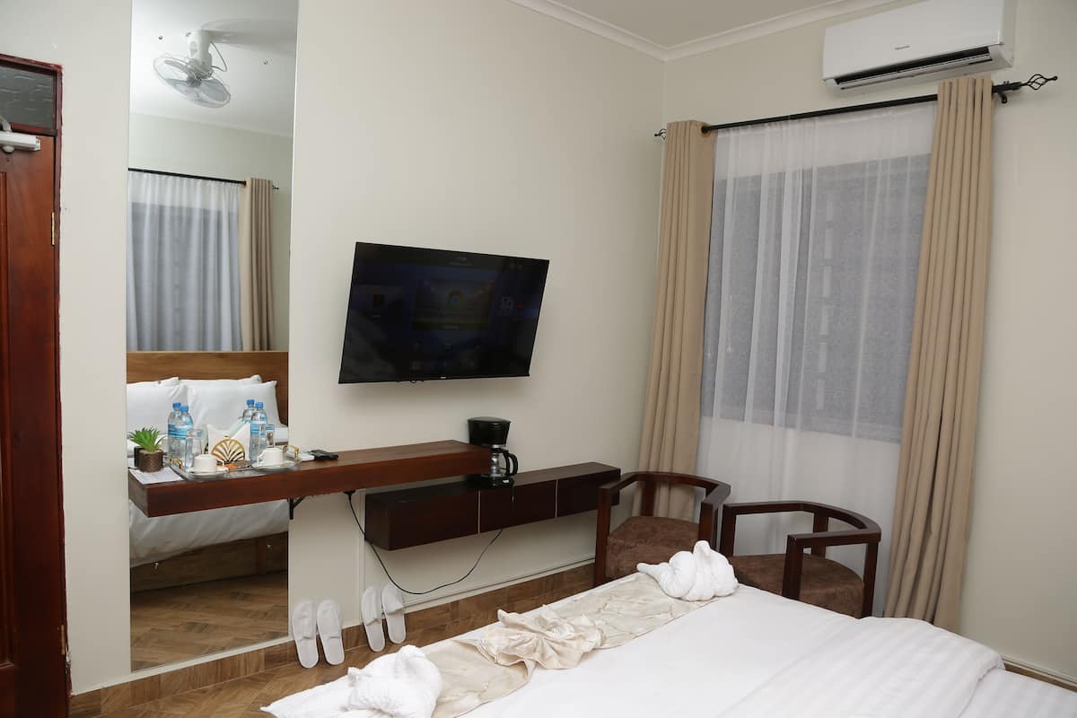 A hotel room with a bed, a TV mounted on the wall, a desk with a coffee maker, and a window with curtains.