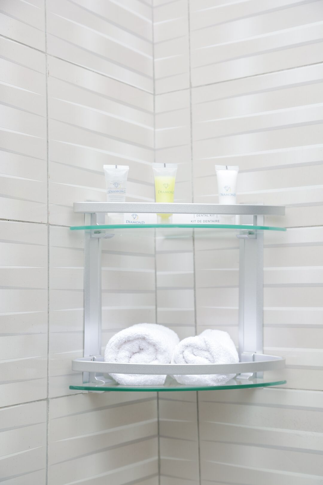 Un baño con repisas de vidrio que sostienen un kit dental y dos toallas enrolladas.