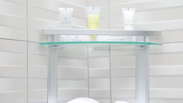 Un baño con repisas de vidrio que sostienen un kit dental y dos toallas enrolladas.
