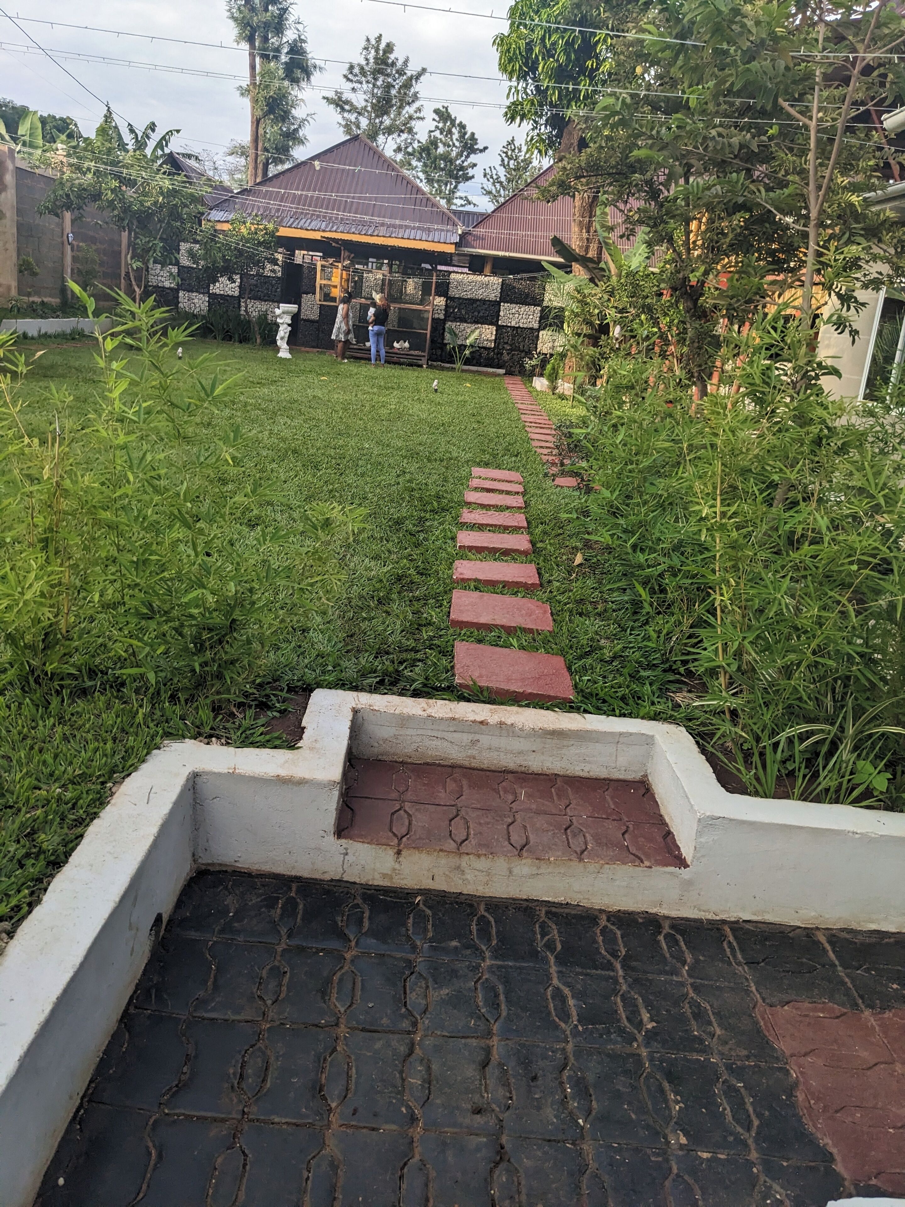 A pathway leading to a building with a tiled roof and a small garden area with grass and plants.